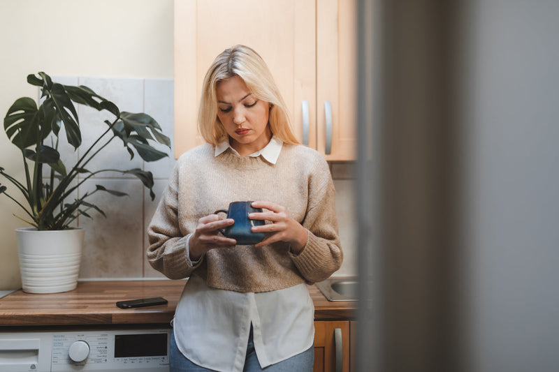 Femme dans sa cuisine, une tasse entre les mains